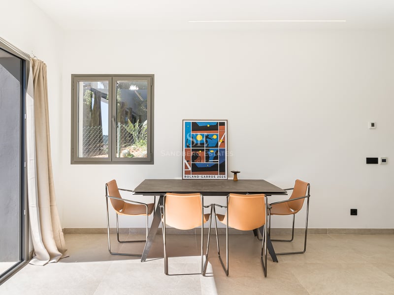 Modernt matrum med stenbord, läderstolar i cognac och stora skjutdörrar i glas mot en terrass.