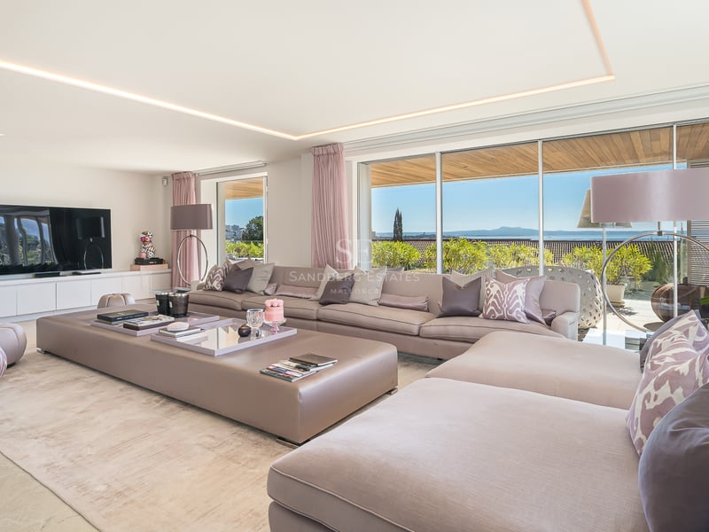 Geräumiges Wohnzimmer mit taupefarbenem Sofa und bodentiefen Fenstern mit Blick auf Garten und Meer.