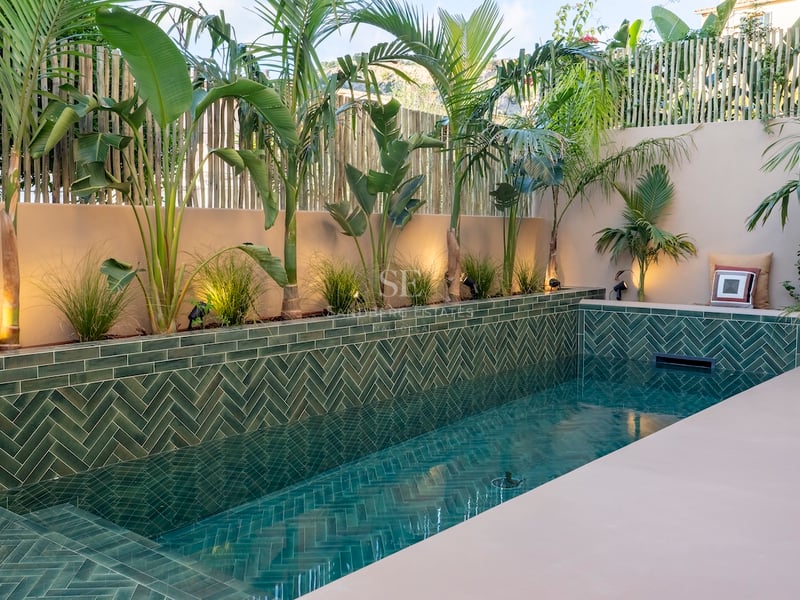 Piscine de luxe avec carreaux verts en chevrons, palmiers et murs beiges avec un éclairage chaleureux.