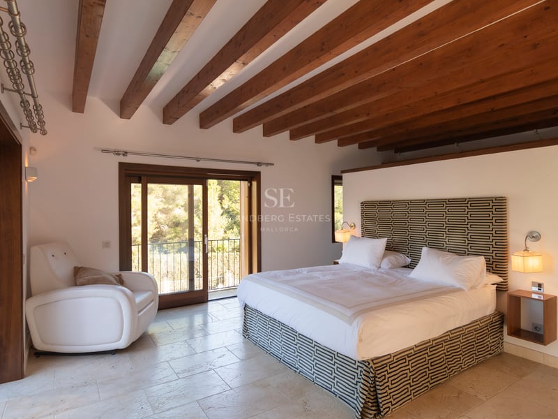 Huvudsovrum med rustika takbjälkar i trä, naturstensgolv och utgång till balkong.