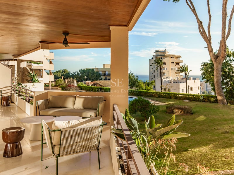 Überdachte Terrasse mit modernen Sofas, Holzdecke und Deckenventilator mit Blick auf einen Garten und das Meer.