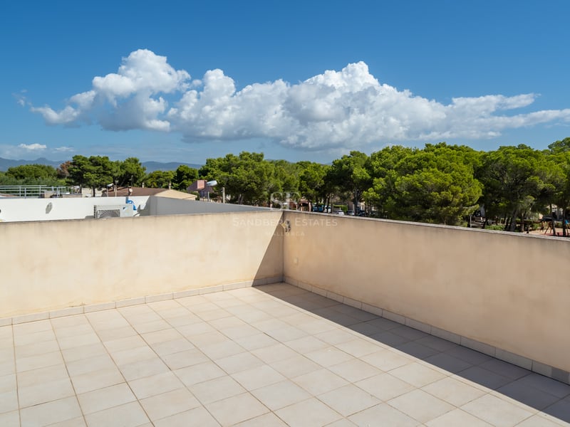 Tom takterrass med beige klinker och låga murar med utsikt över en tallskog under en blå himmel.