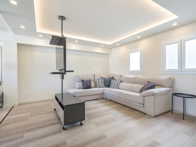 Modernes Wohnzimmer mit beige Ecksofa, hellem Holzboden und minimalistischer schwarzer TV-Halterung.