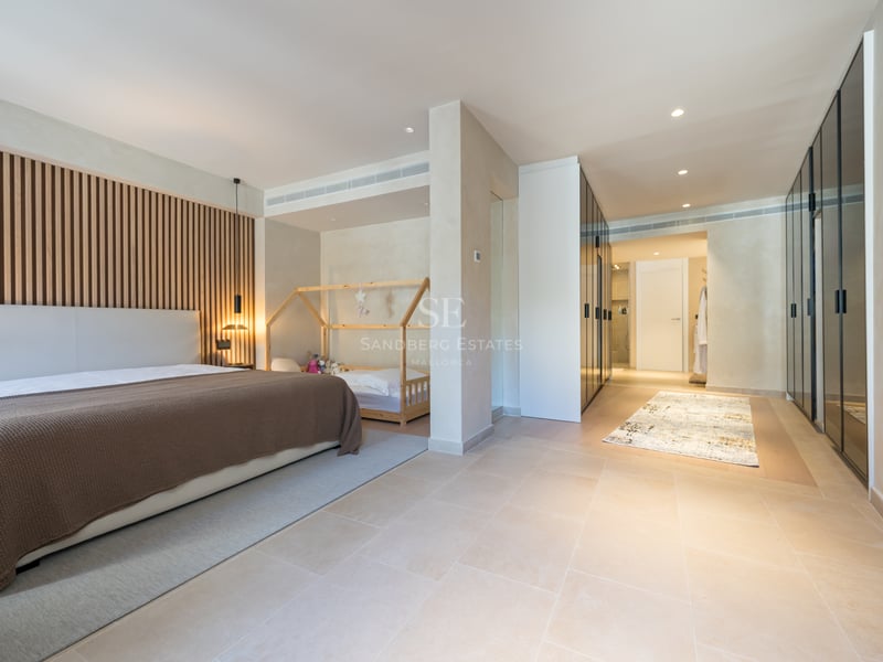 Chambre principale moderne avec tête de lit en lattes de bois, sol en pierre et placards en verre noir.