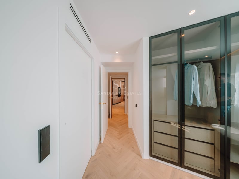 Couloir moderne avec parquet en chevrons menant à un dressing doté de portes vitrées aux cadres noirs.