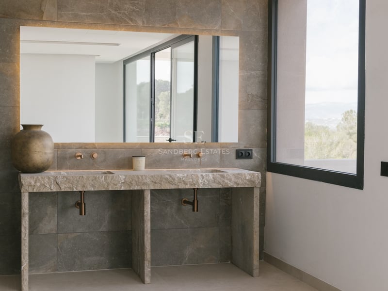 Modernes Badezimmer mit Doppelwaschbecken aus Rohstein, Wandarmaturen aus Bronze und hinterleuchtetem Spiegel.