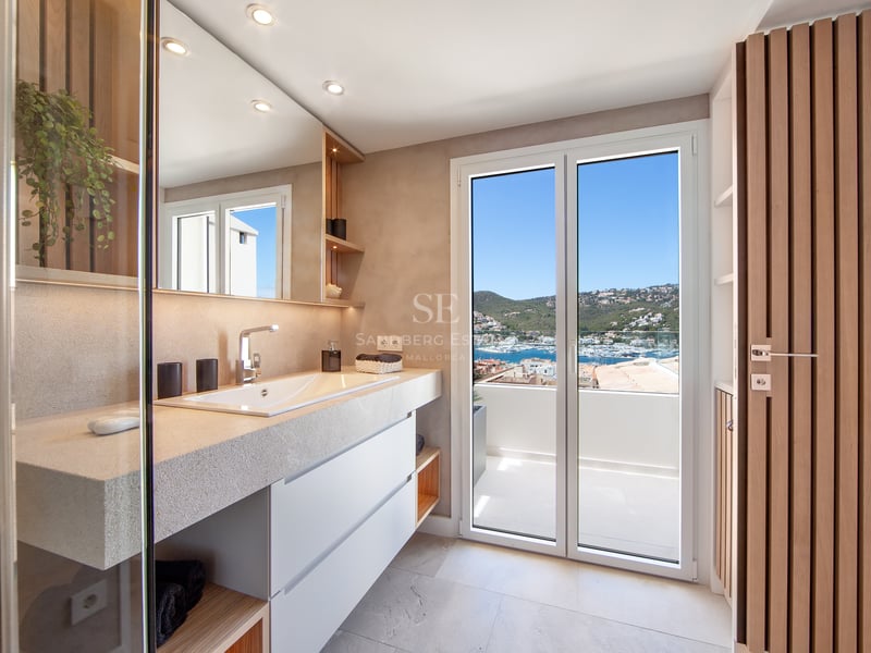 Salle de bain moderne avec vanité en pierre, grand miroir et portes vitrées ouvrant sur un balcon avec vue sur la marina.