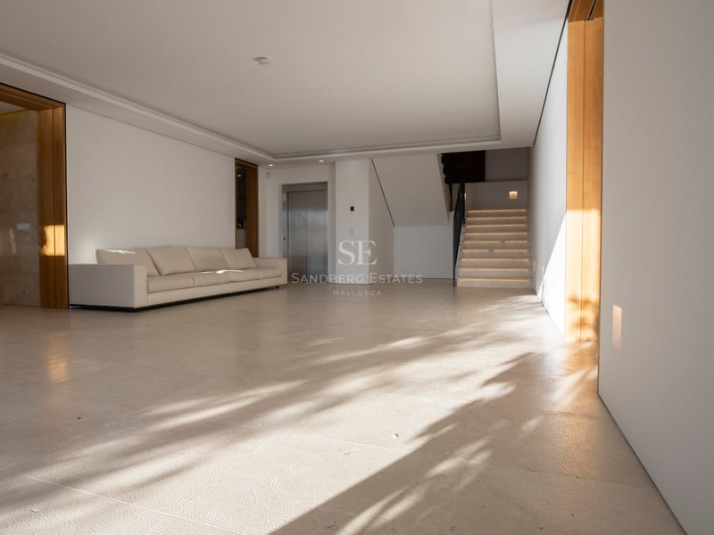 Großzügige minimalistische Halle mit cremefarbenen Steinböden, weißem Sofa, privatem Aufzug und Steintreppe.