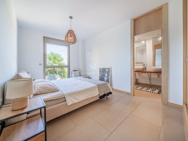 Chambre lumineuse avec accents de bois clair, salle de bains attenante et vue sur les palmiers.