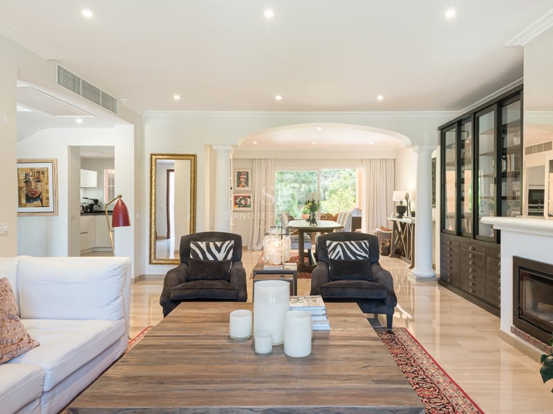 Bright open-plan living room featuring a marble floor, fireplace, and large windows leading to a lush garden terrace.
