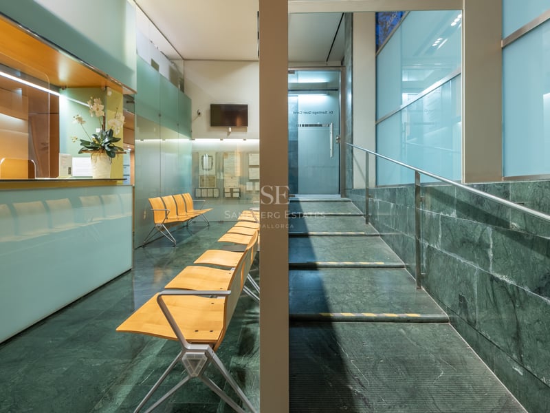 Espace de réception avec sol en marbre vert, chaises en bois, parois en verre dépoli et escalier en acier.