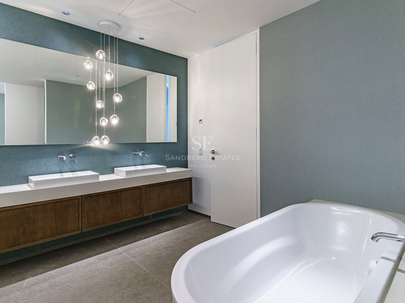 Salle de bain de luxe avec baignoire blanche, meuble double vasque en bois et suspensions boules en verre.