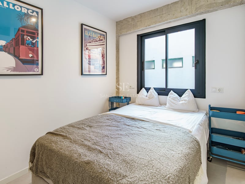 Chambre moderne avec lit double, poutres en béton, dessertes bleues et affiches de voyage vintage.