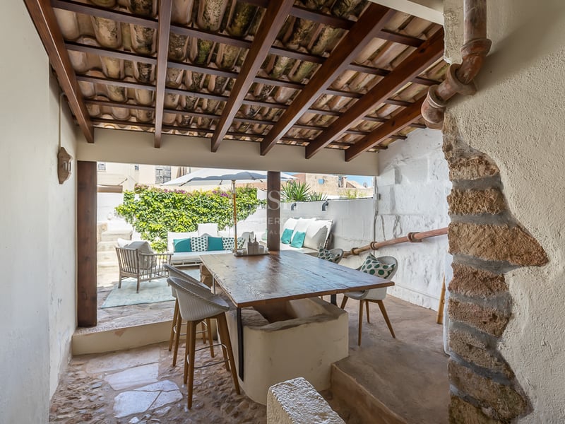 Terrasse méditerranéenne couverte avec grande table en bois, poutres apparentes et salon extérieur lumineux.