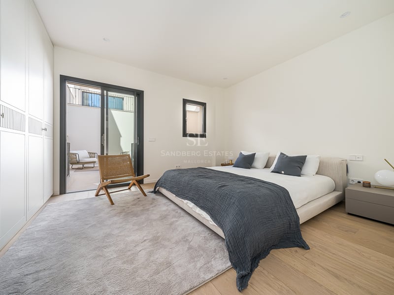 Modern bedroom with large bed, floor-to-ceiling white wardrobes, light oak flooring, and sliding glass door to a terrace.