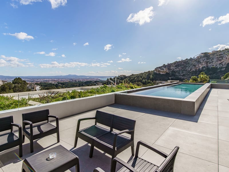 Terrasse de luxe avec piscine à débordement, garde-corps en verre, meubles noirs et vue panoramique.