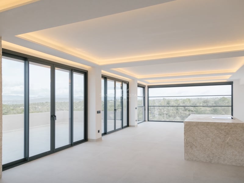 Moderner Küchenbereich mit einer massiven Kochinsel aus Naturstein und bodentiefen Fenstern mit Ausblick.