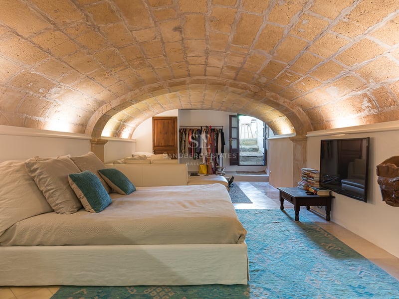 Chambre avec plafond voûté en pierre naturelle, grand lit avec touches de turquoise et éclairage indirect chaleureux.