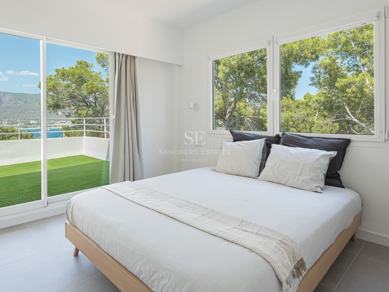 Chambre moderne avec lit double et baies vitrées ouvrant sur une terrasse avec vue sur mer et montagne.