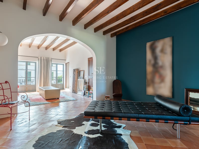 Salon intérieur avec carreaux de terre cuite, poutres apparentes, mur d'accent bleu canard et banquette en cuir noir.