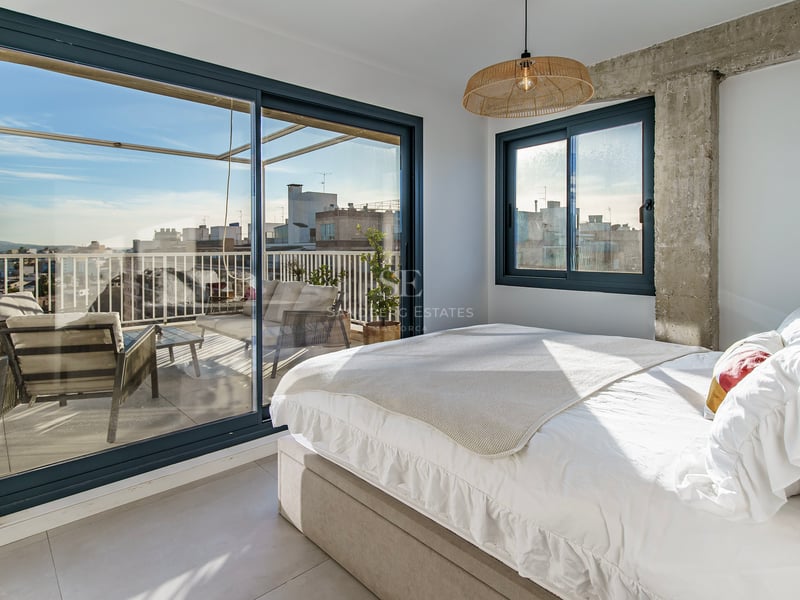Chambre lumineuse avec lit blanc et grandes baies vitrées coulissantes ouvrant sur une terrasse privée avec vue.