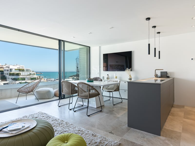 Heller Wohnbereich mit Esstisch, Kücheninsel und Glastüren, die auf eine Terrasse mit Meerblick führen.