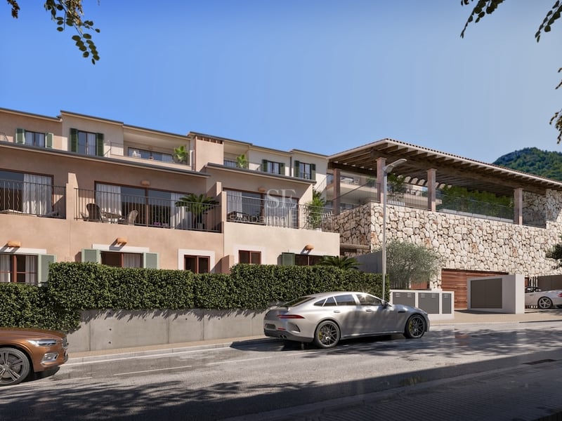 Exterior view of a multi-story modern Mediterranean villa with stone walls, balconies, and green hedges under a blue sky.