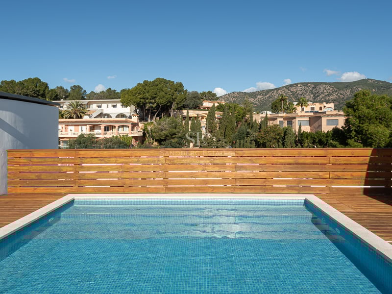 Une piscine rectangulaire sur le toit avec des carreaux bleus et une terrasse en bois, surplombant des collines vertes.