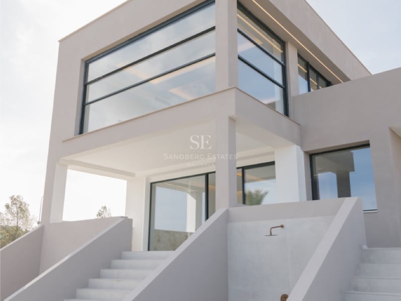 Moderne Villa mit großen Glasfronten und minimalistischen weißen Betontreppen unter hellem Himmel.