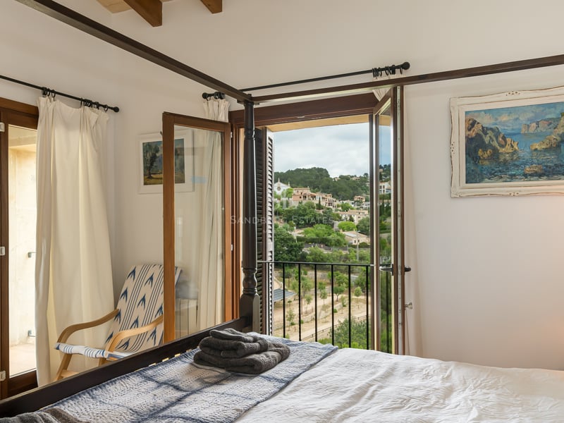Chambre de style méditerranéen avec un lit à baldaquin en bois sombre et balcon offrant une vue sur les collines.