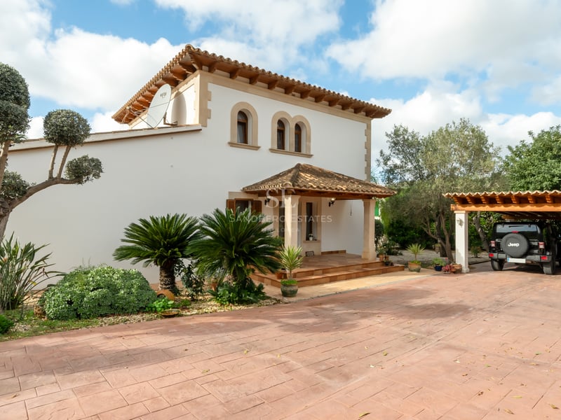 Two-story white Mediterranean villa with terracotta roof, arched windows, and a wide driveway with a carport.