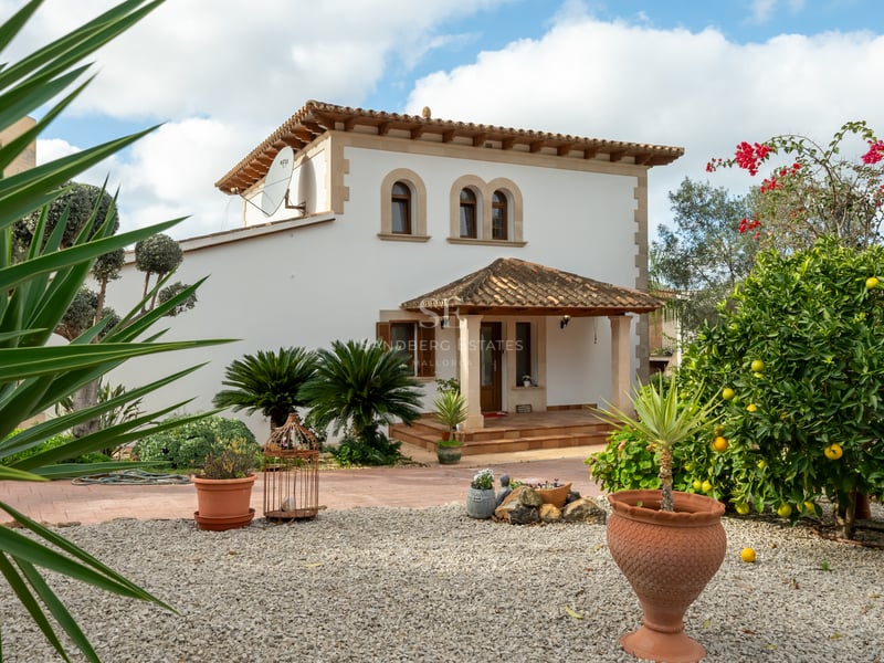 White two-story villa with terracotta roof, arched windows, and a landscaped garden featuring lemon trees and gravel.