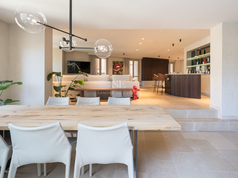 Table à manger en bois clair et chaises blanches dans un espace ouvert avec sol en pierre et luminaire design.