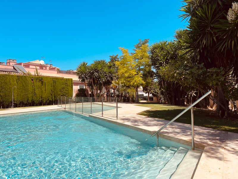 Vue rapprochée d'une piscine aux eaux turquoises, terrasse en pierre et clôture en verre, bordée de palmiers.