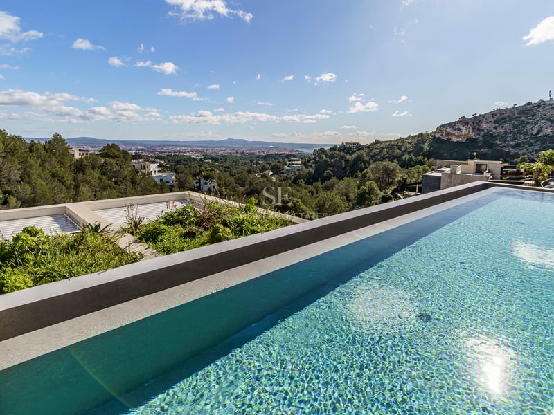 Une piscine à débordement à l'eau bleue claire surplombant une vallée verdoyante et une ville lointaine.