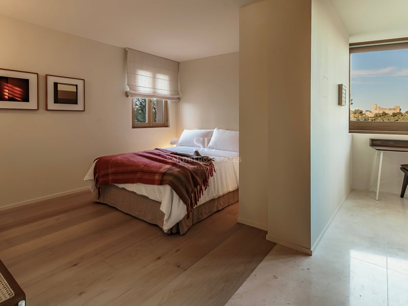 Minimalistisches Schlafzimmer mit weißem Bett, Holzböden und Arbeitsbereich mit Blick auf eine historische Burg.