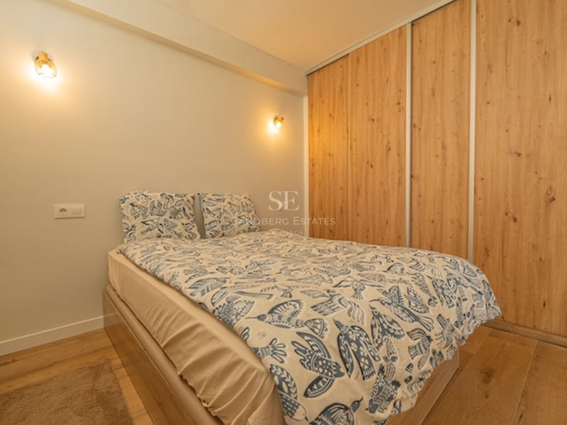 Dormitorio moderno con cama de textiles azules, armarios empotrados de madera de roble e iluminación de pared cálida.