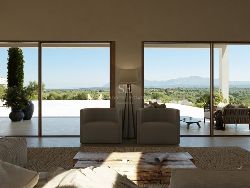 Salon minimaliste avec de grandes baies vitrées ouvrant sur une terrasse surplombant la vallée et les montagnes.