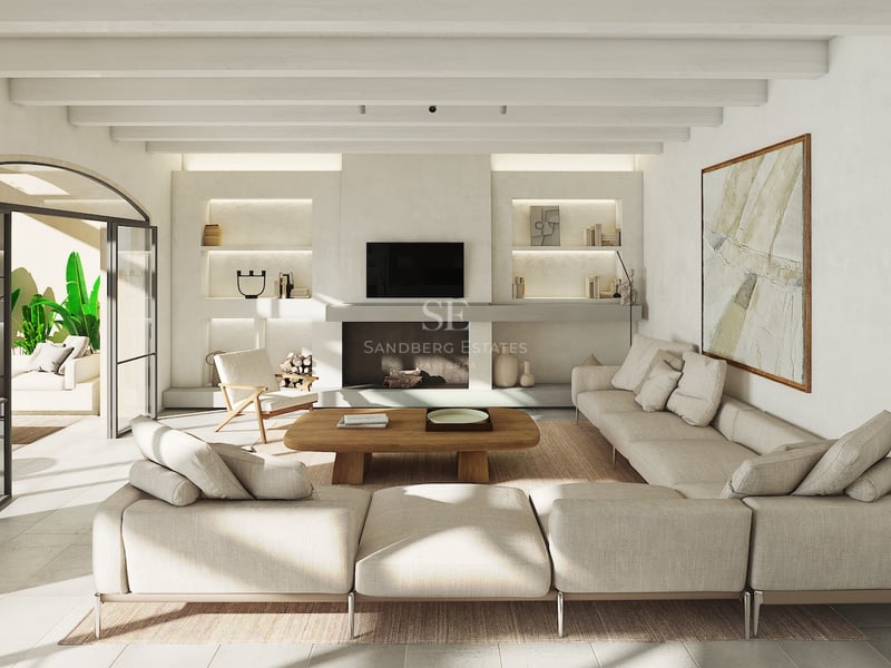 Salon baigné de lumière avec canapé beige, poutres apparentes et accès à une terrasse via une porte voûtée.