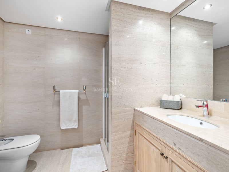 Salle de bain moderne avec murs en pierre beige, bidet blanc, meuble en bois avec lavabo et grand miroir.