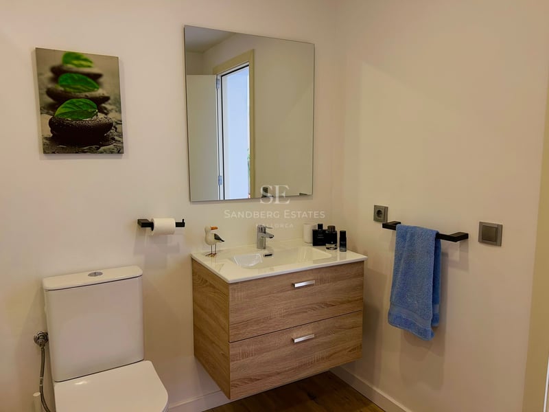 A modern bathroom featuring a floating wood vanity, white toilet, and minimalist decor.