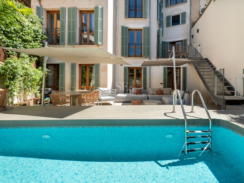 Piscine turquoise avec échelle devant une façade blanche aux volets verts et salon de jardin.
