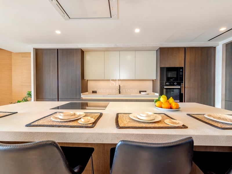 Cuisine moderne avec un grand îlot en pierre, des armoires en bois sombre et des appareils électroménagers intégrés.