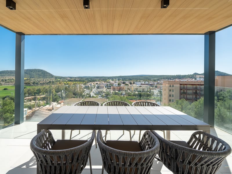 Terrasse moderne avec plafond en bois, table à manger et garde-corps en verre donnant sur une vallée verdoyante.