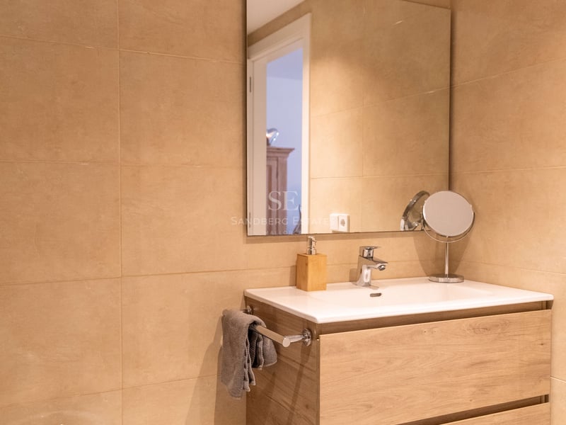 Modernes Bad mit schwebendem Eichen-Waschtisch, weißem Keramikbecken, großem Spiegel und sandfarbenen Fliesen.