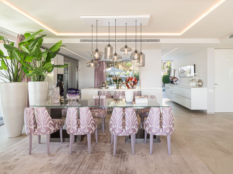 Moderner Essraum mit Glastisch, gemusterten lavendelfarbenen Stühlen und Designer-Glaspendelleuchten.