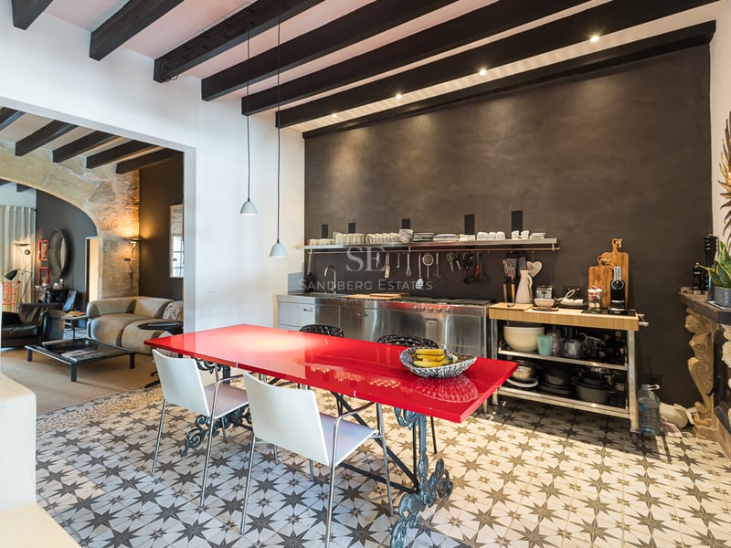 Cuisine industrielle moderne avec table rouge vif, sol en carreaux de ciment et poutres en bois sombre apparentes.