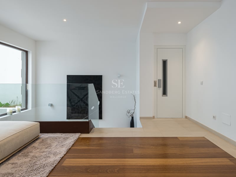 Palier moderne avec garde-corps en verre, parquet en chêne et porte d'ascenseur blanche.