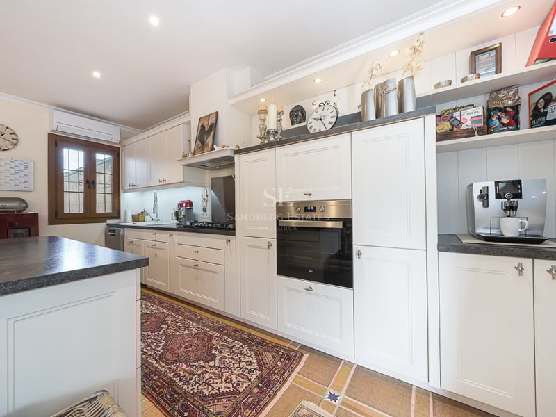 Cuisine blanche avec plans de travail sombres, four encastré et tapis de style oriental sur sol carrelé.