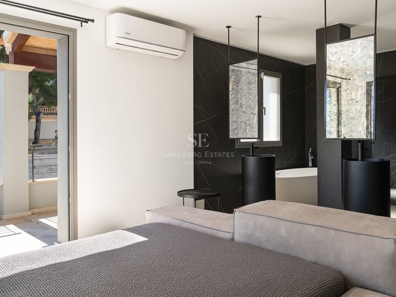 Lyxigt sovrum med öppet badrum i svart marmor, pelartvättställ och utgång till solig terrass.